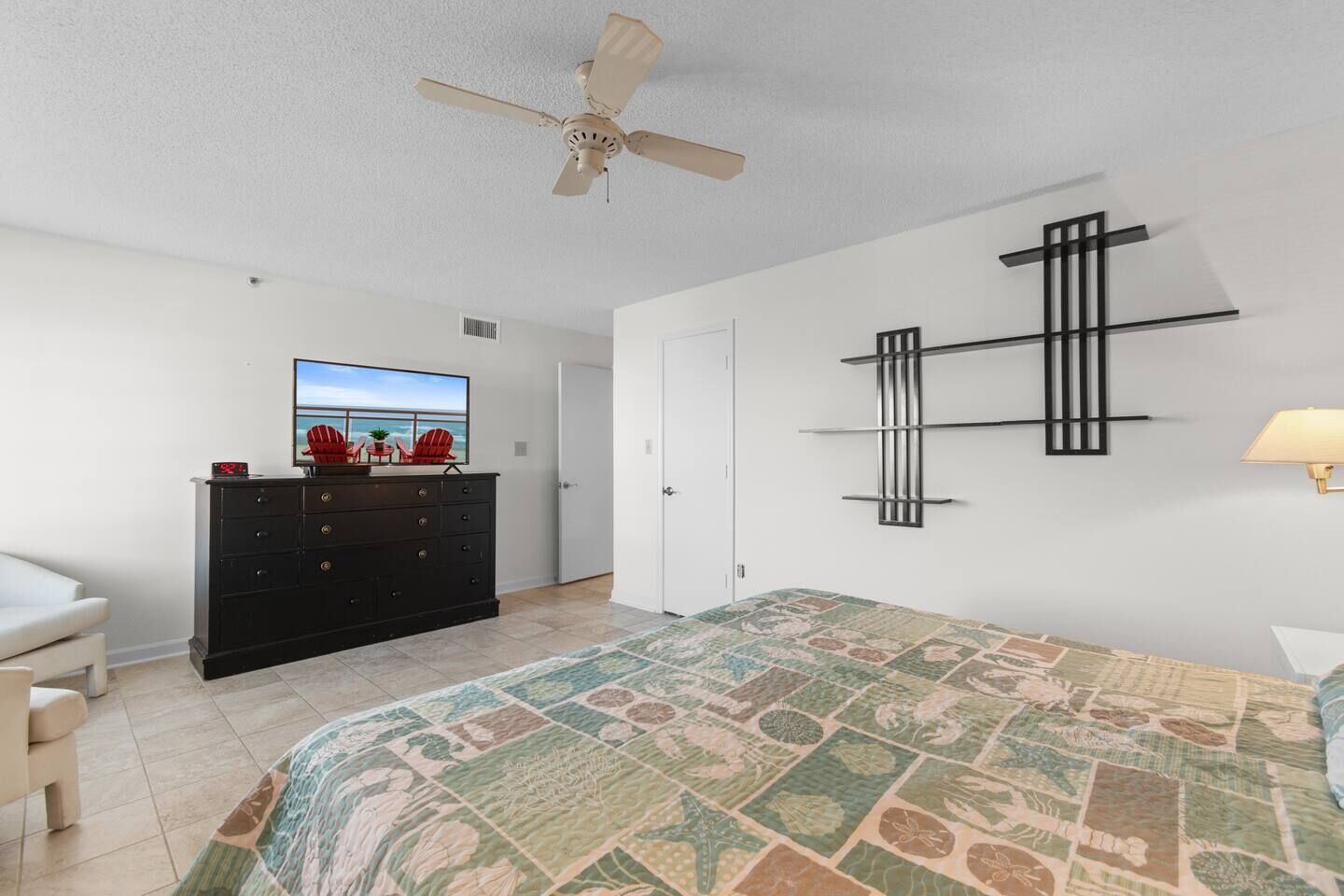 A bedroom with a bed, a dresser, a television, a ceiling fan, and a wall-mounted shelf.