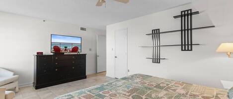 A bedroom with a bed, a dresser, a television, a ceiling fan, and a wall-mounted shelf.