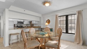 Una cocina moderna con armarios blancos, microondas y comedor con mesa de vidrio y sillas de madera.