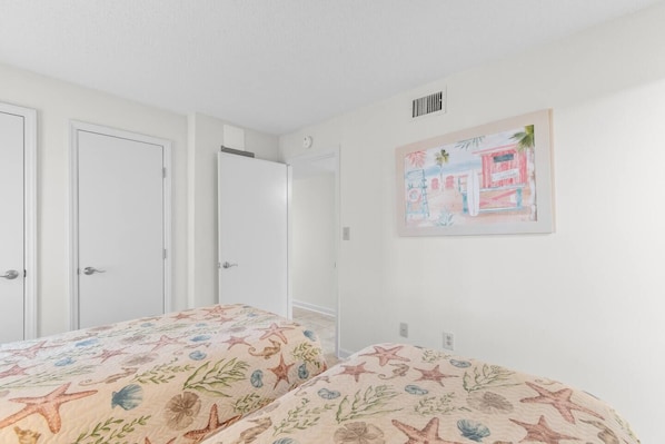 A bedroom with two beds, white walls, a door, and a framed picture on the wall. - 3 Bdrm @ Sea marsh II-pool- corner oceanfront view (North Myrtle Beach)