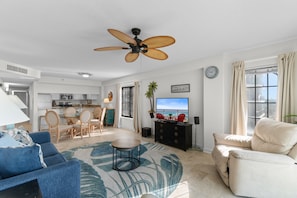 Un salon doté d’un ventilateur de plafond, d’un téléviseur, d’un canapé, d’une table basse et offrant une vue sur l’océan par une fenêtre.
