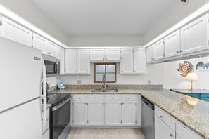A kitchen with white cabinets, a granite countertop, a built-in oven, a microwave, a sink, and a coffee maker. - 3 Bdrm @ Sea Marsh II-Pool- Corner Oceanfront View (North Myrtle Beach)