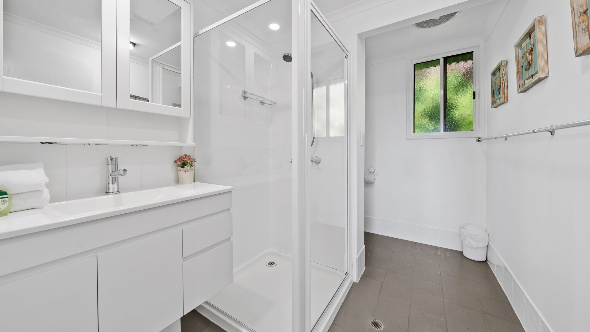 A modern bathroom with a white vanity, a glass shower enclosure, and a window with a view of greenery.