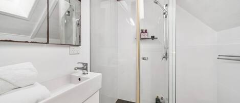Ein modernes Badezimmer mit einer gläsernen Duschkabine, einem weißen Waschtisch mit Spiegel und einem Handtuchhalter.
