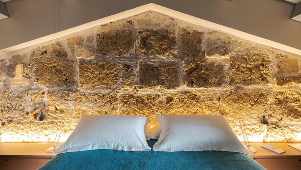 A bedroom with a stone wall, a bed with white pillows, and a blue blanket.