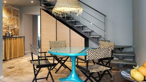 A dining area with a glass table and chairs, a hanging light fixture, and a staircase.