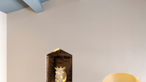 A modern interior with a minimalist design, featuring a staircase with a glass railing, a small illuminated sculpture, and a recessed wall light.
