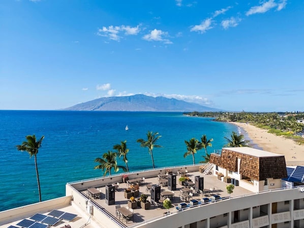 A rooftop terrace with seating and a view of the ocean and a mountain.