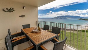A balcony with a wooden table and chairs, overlooking a beach with clear skies. - Royal Mauian 503-Oceanfront with AC (Kihei)