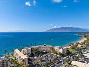 A hotel with a curved building, a parking lot, and a view of the ocean and beach.