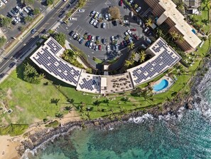 An aerial view of a hotel with a circular parking lot, a swimming pool, and a beachfront.