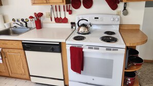 Una cocina con armarios de madera, una estufa blanca, un lavavajillas y varios utensilios de cocina.