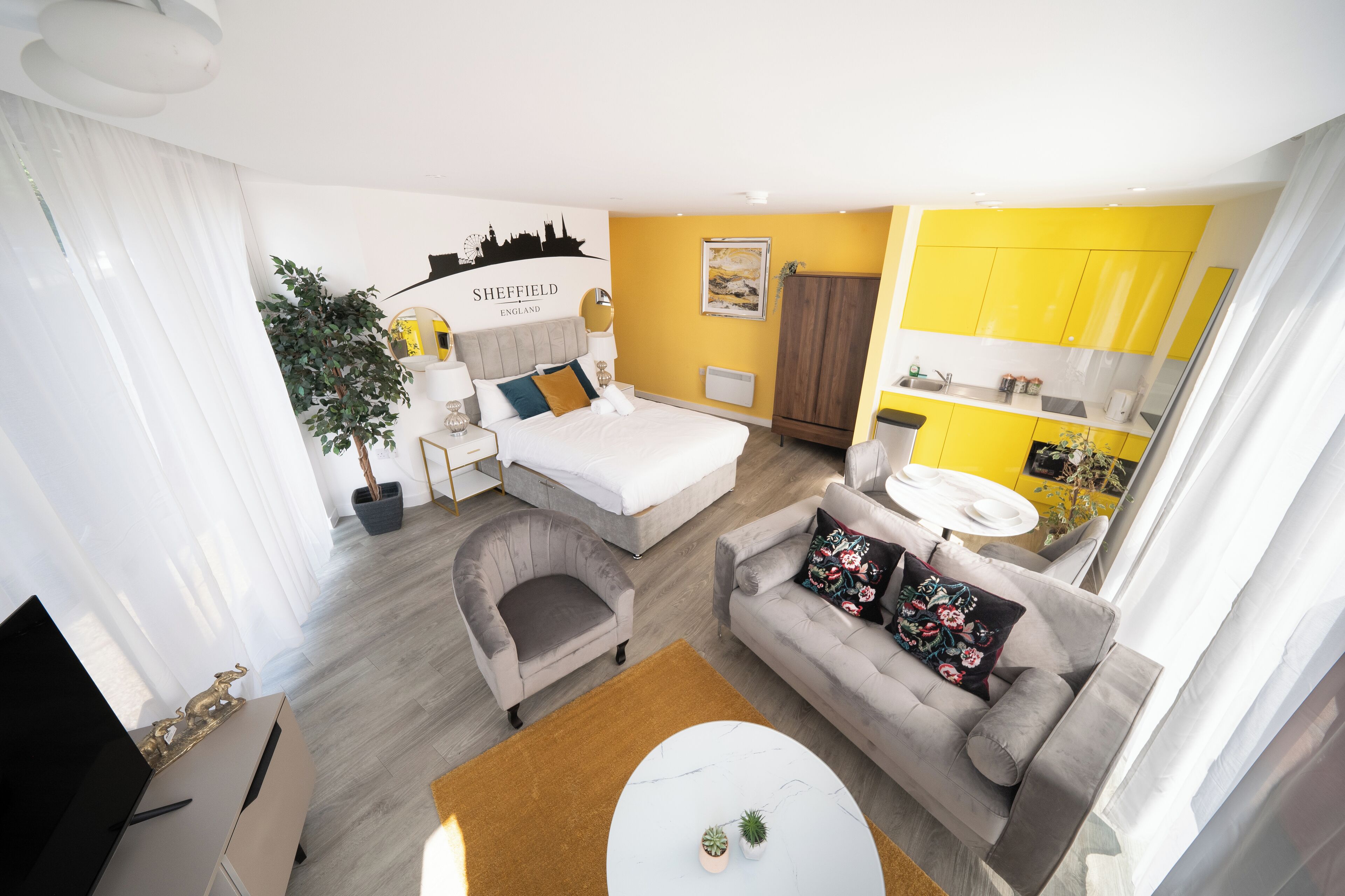 Una habitación de hotel moderna con cama, dos sofás, una mesa de centro, un escritorio y un comedor con armarios amarillos.