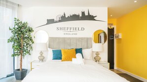Una habitación de hotel con una cama, un cuadro de la silueta urbana, una planta en maceta y un espejo.