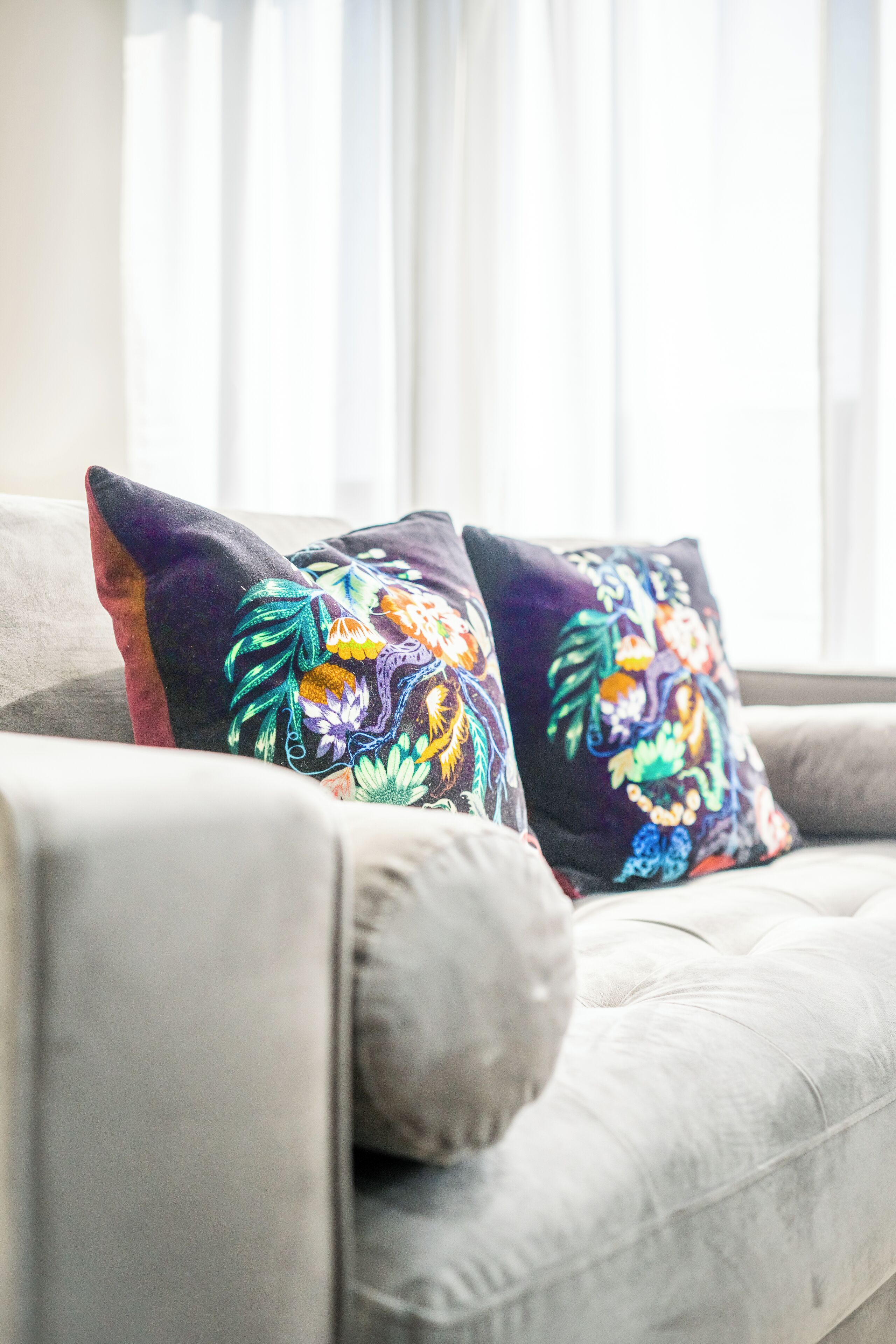 Un sofá gris con dos cojines decorativos con bordados florales.