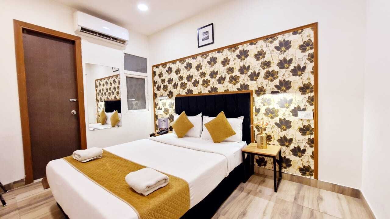 A hotel room with a large bed, a bedside table, a mirror, and a floral-patterned headboard.