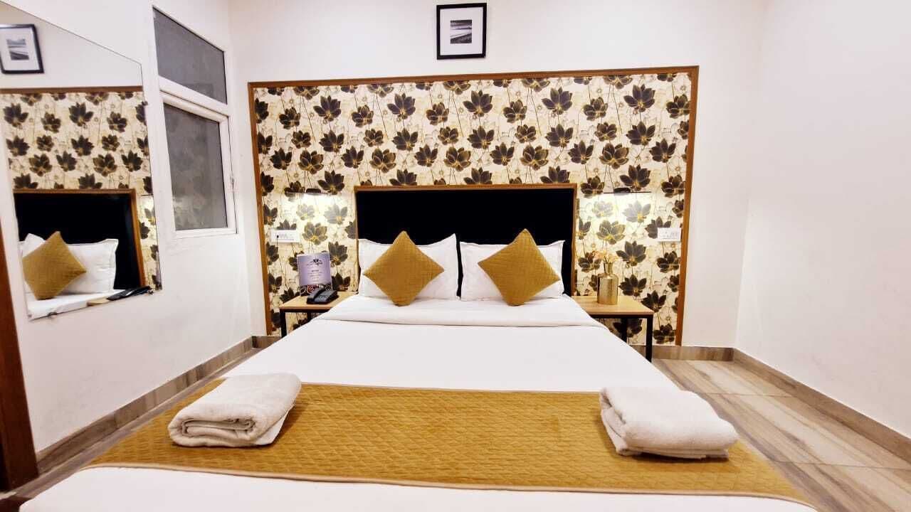 Habitación de hotel con una cama grande, dos mesitas de noche, un cabecero con papel tapiz floral y una ventana.
