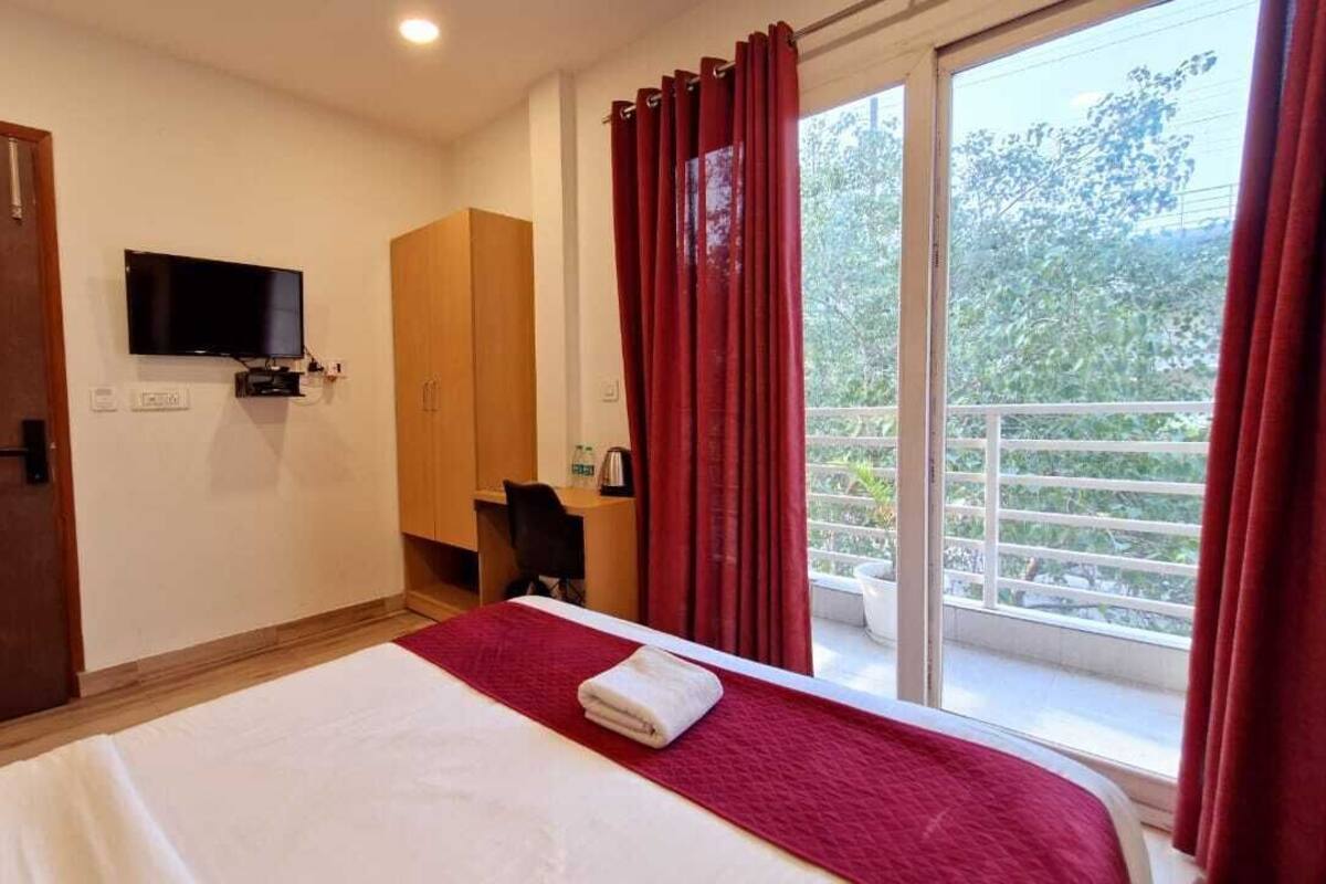 Habitación de hotel con cama, televisor montado en la pared, armario y balcón con cortinas rojas.