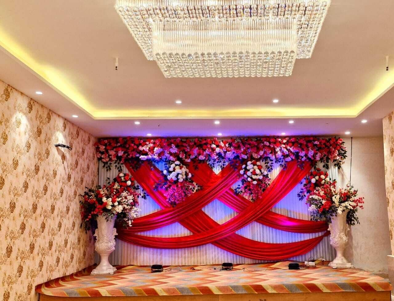 A stage with red drapes, floral arrangements, and a chandelier.