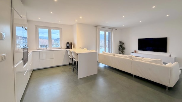 A modern apartment with a kitchen, dining area, and living room. It features large windows, a flat-screen TV, and a white sofa. - Modern Green & White - Apartment T3 60m2 Annecy - Parking Privé - Wifi - Netflix (Annecy)