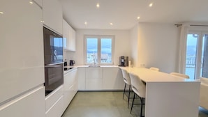 A modern kitchen with white cabinetry, a built-in oven, a coffee machine, and a window overlooking a cityscape. - Modern Green & White - Apartment T3 60m2 Annecy - Parking Privé - Wifi - Netflix (Annecy)