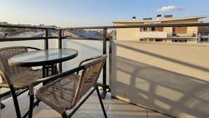 A balcony with a round table and wicker chairs, overlooking a cityscape with buildings and a clear sky. - Modern Green & White - Apartment T3 60m2 Annecy - Parking Privé - Wifi - Netflix (Annecy)