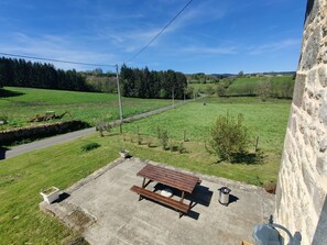 A picnic table with benches and a trash can in a grassy area with a stone wall and a stone building in the background. - House in the Livradois-Forez Nature Park. (Grandval)