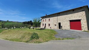 Un bâtiment en pierre avec une porte de garage rouge, entouré d’une pelouse et d’arbres.