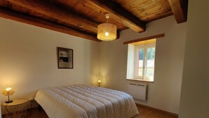 Une chambre avec un grand lit, un plancher en bois, un ventilateur de plafond, une fenêtre et un radiateur fixé au mur.