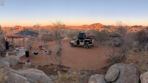 A desert campsite with a vehicle, a covered seating area, and a small structure. - Ozohere Campsite and Himba Village (Uis)