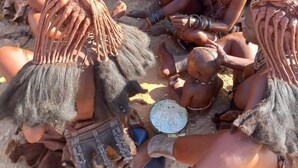 A group of people sitting around a fire in an outdoor setting with a natural, earthy background. - Ozohere Campsite and Himba Village (Uis)