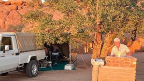 A white pickup truck parked beside a tent and a brick structure with a person standing next to it. - Ozohere Campsite and Himba Village (Uis)