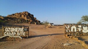 An entrance to Ozohere Camp Site with a stone sign and a mural of a person holding a tent and a shovel. - Ozohere Campsite and Himba Village (Uis)