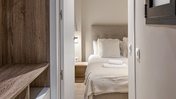 Quarto com guarda-roupa de madeira, cama com roupa de cama branca e mesa de cabeceira.