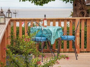 Eine Holzterrasse mit Tisch und Stühlen, einer Weinflasche und Blick auf das Meer.