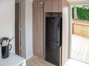 Una cocina compacta con un refrigerador negro empotrado, un mueble de madera y una pequeña encimera con cafetera.