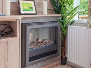 Una chimenea con leña, un cuadro enmarcado encima y una planta en maceta a un lado.