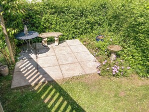 Eine Terrasse mit Steintisch und Bank, umgeben von Grünpflanzen und einem kleinen Vogelbad.