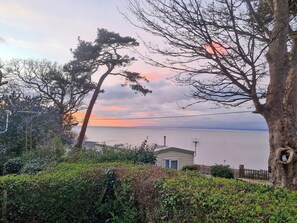 Eine Küstenlandschaft mit einem Haus, dichtem Grün und freiem Blick auf das Meer.