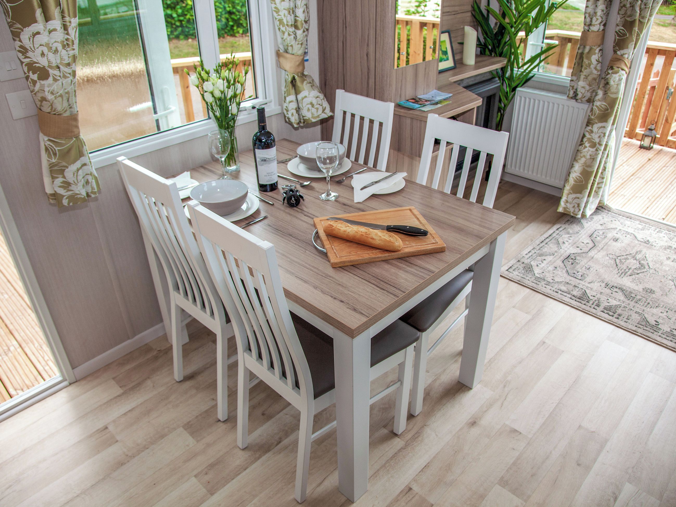 A dining table with chairs, a bottle of wine, a bread roll, and a cutting board.