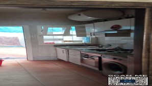 A kitchen with a stove, sink, and cabinets. There is a red bucket on the floor and a window with curtains. - Appartement a Louer au Nord du Maroc Fnideq (Fnideq)