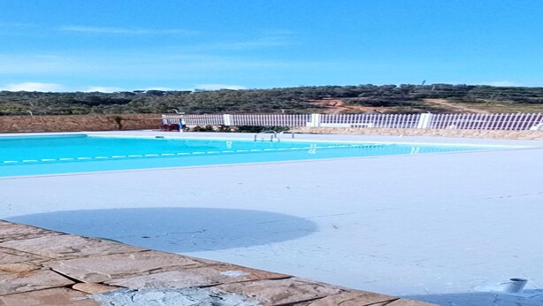 A swimming pool with clear blue water, surrounded by a white deck and stone walls. - Appartement a Louer au Nord du Maroc Fnideq (Fnideq)