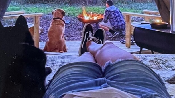 Une tente avec un feu au centre, un chien et une personne assise par terre.