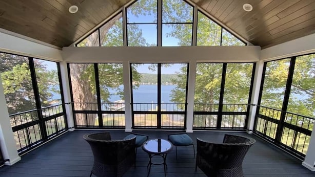 A covered outdoor deck with a view of a lake, furnished with wicker chairs and a small table. - BRAND NEW 7 BR / 5 BA luxury home ON Keuka Lake just outside of Penn Yan! (Penn Yan)