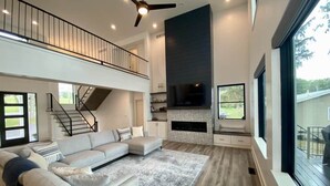 A spacious living room with a large sectional sofa, a fireplace, and a balcony with a railing. - BRAND NEW 7 BR / 5 BA luxury home ON Keuka Lake just outside of Penn Yan! (Penn Yan)