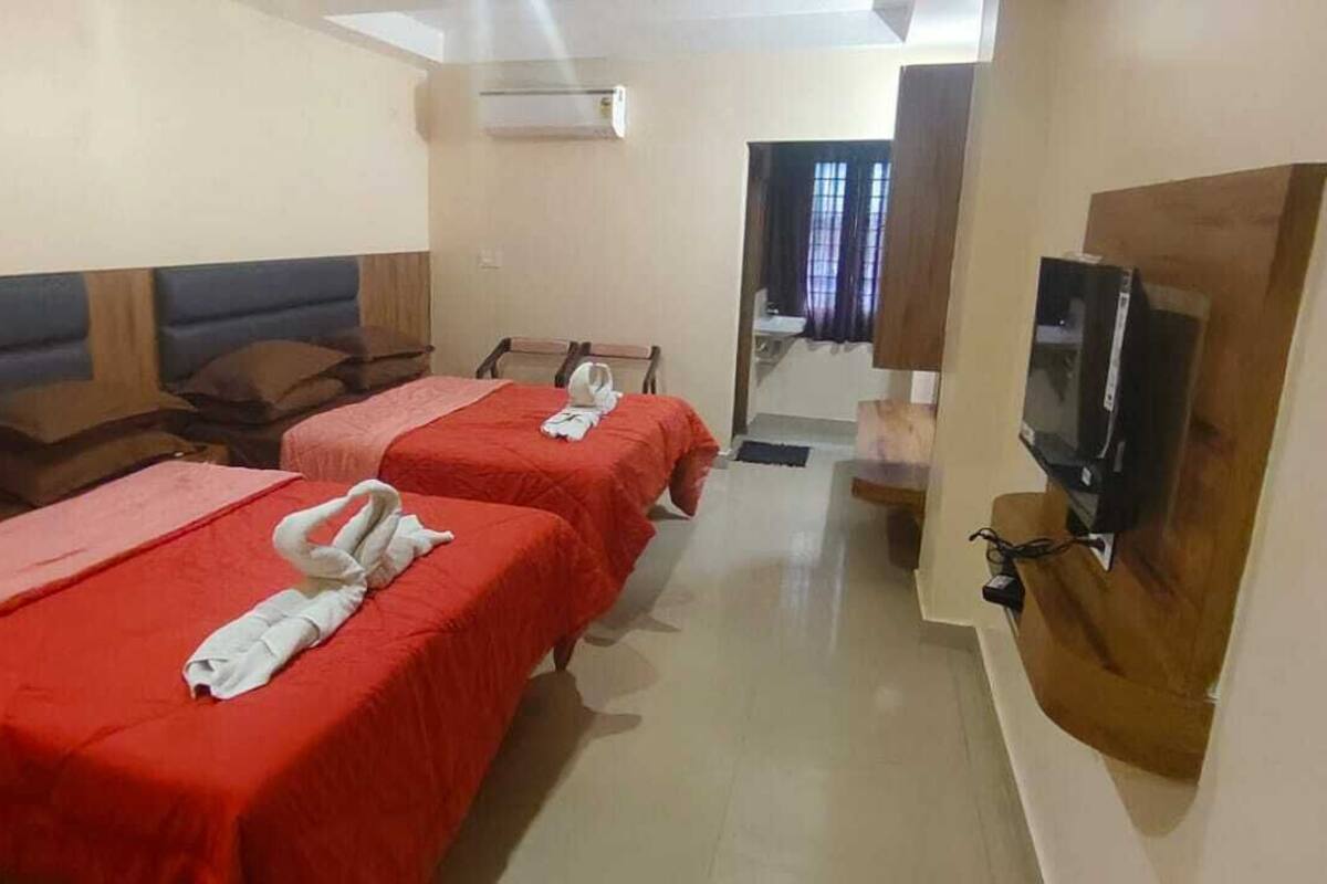 A hotel room with two beds, a TV, and a small bathroom.