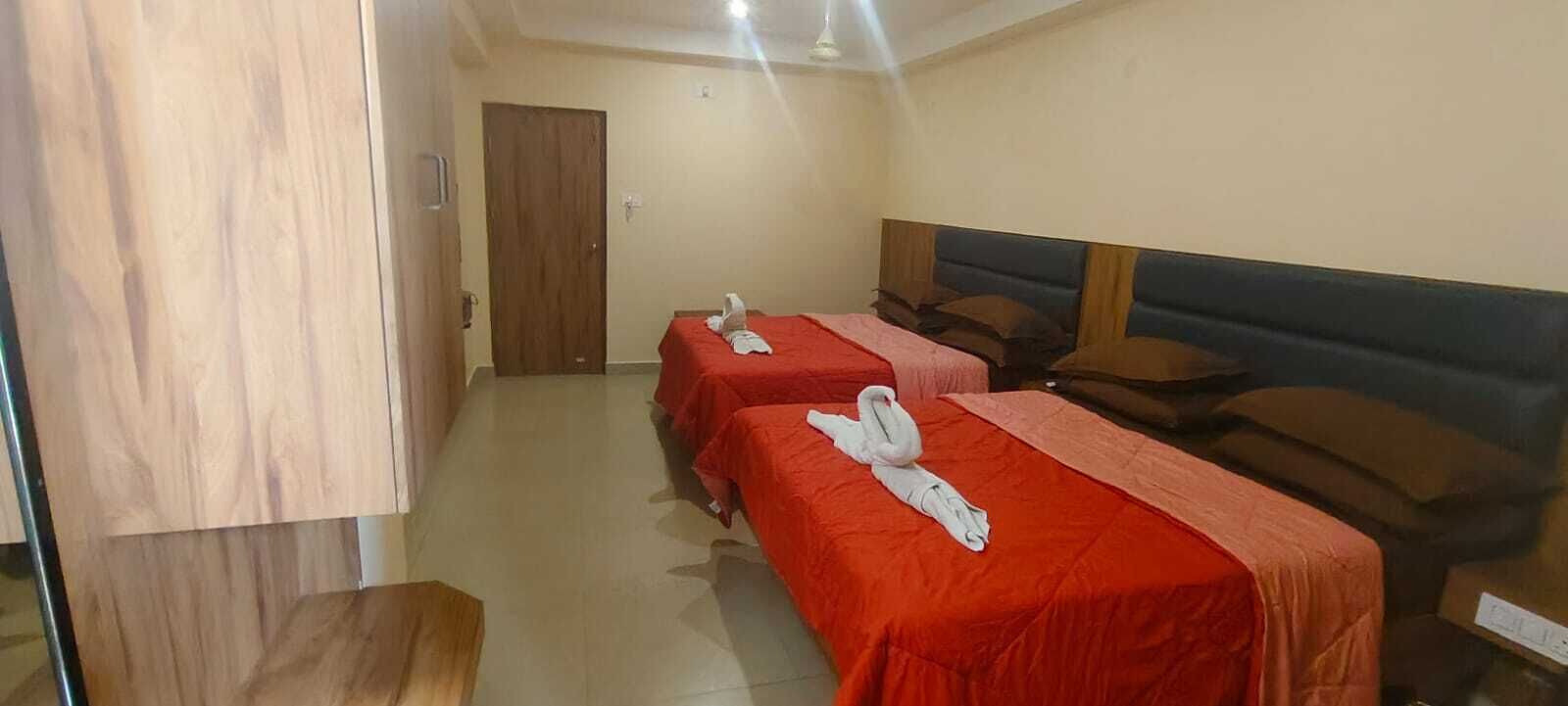 Habitación de hotel con dos camas individuales, cada una con una colcha roja y una toalla blanca.