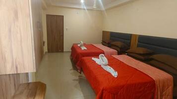 A hotel room with two single beds, each with a red bedspread and a white towel.