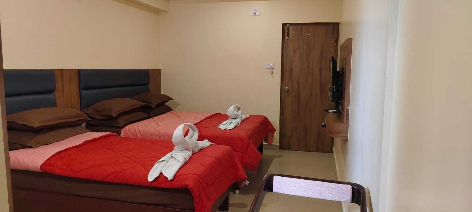 Ett hotellrum med två sängar, var och en med ett rött överkast och vita handdukar. Det finns en sänggavel i trä, en dörr i trä och en tv på ett stativ.