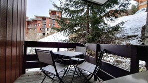 Eine Holzterrasse mit Tisch und Stühlen, mit Blick auf eine verschneite Landschaft und ein mehrstöckiges Gebäude.